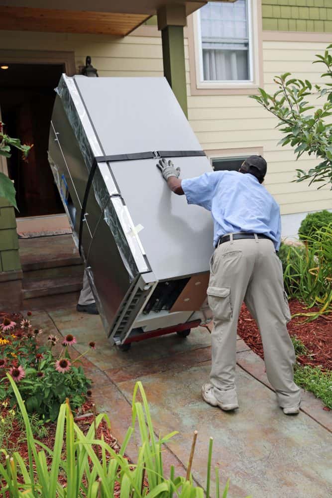 Two moving personnel slowly moving a refrigerator