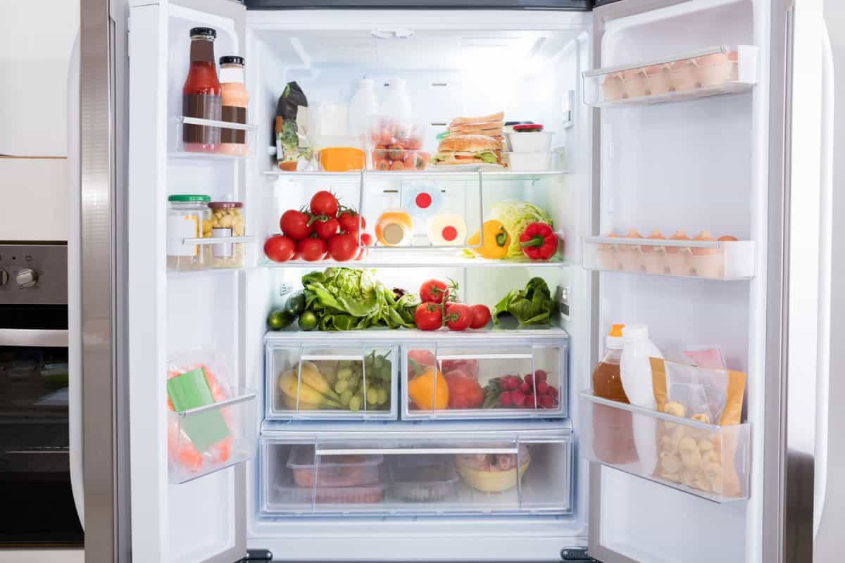 A double door fridge with lots of fruits and eggs on the shelves