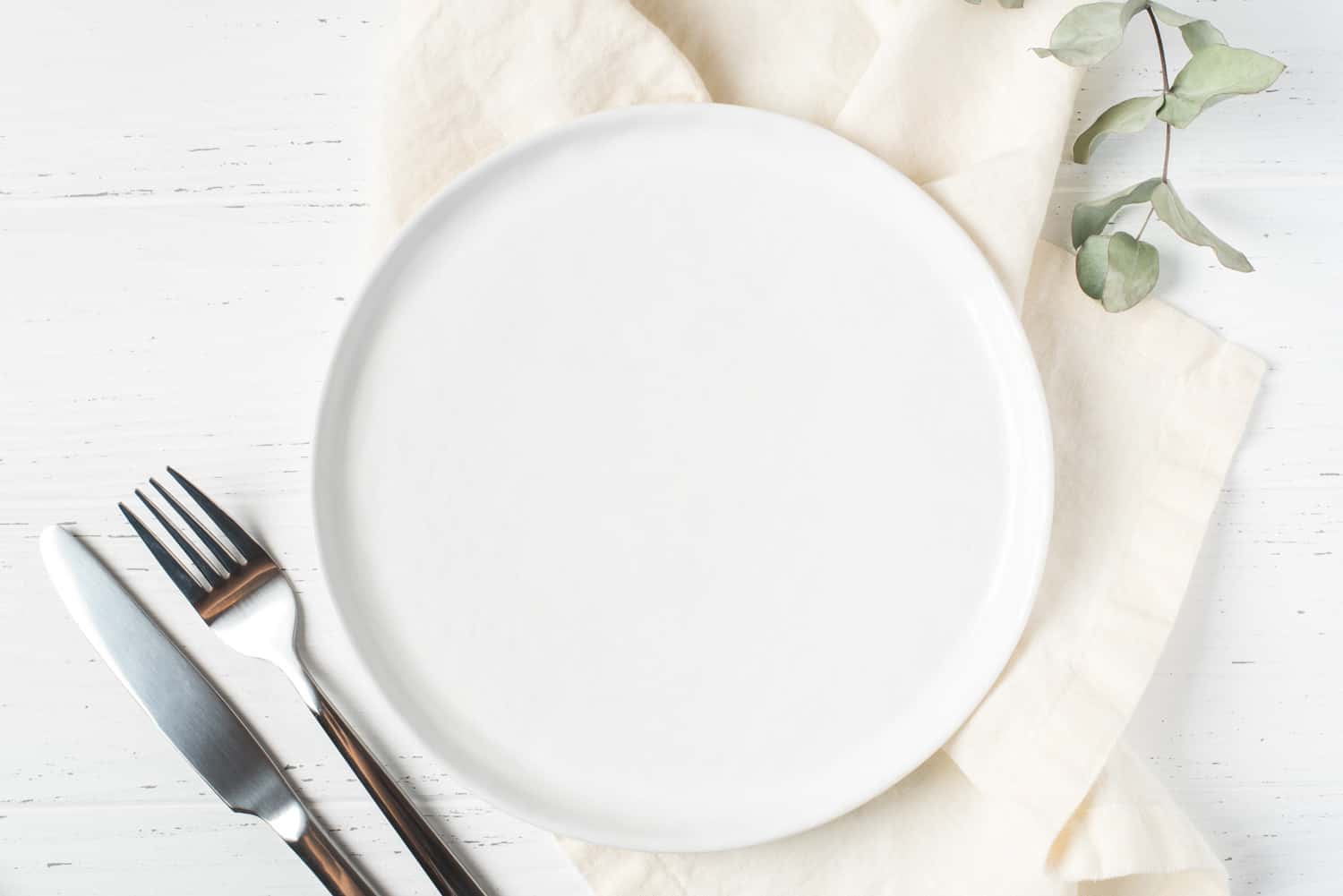 An empty plate and cutlery on a white wooden table. Top view.