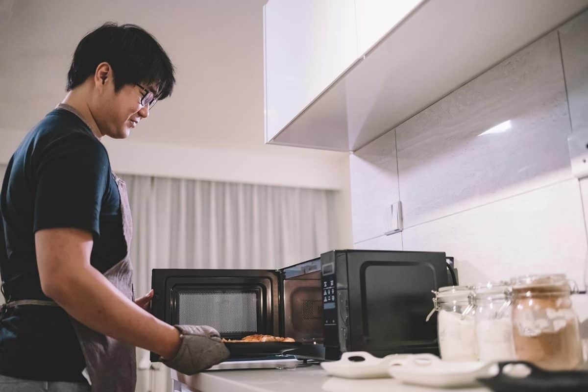An asian chinese male taking a pizza from microwave in the kitchen with glove