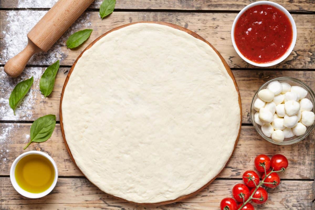 Basic ingredients for a pizza placed on the side of the dough