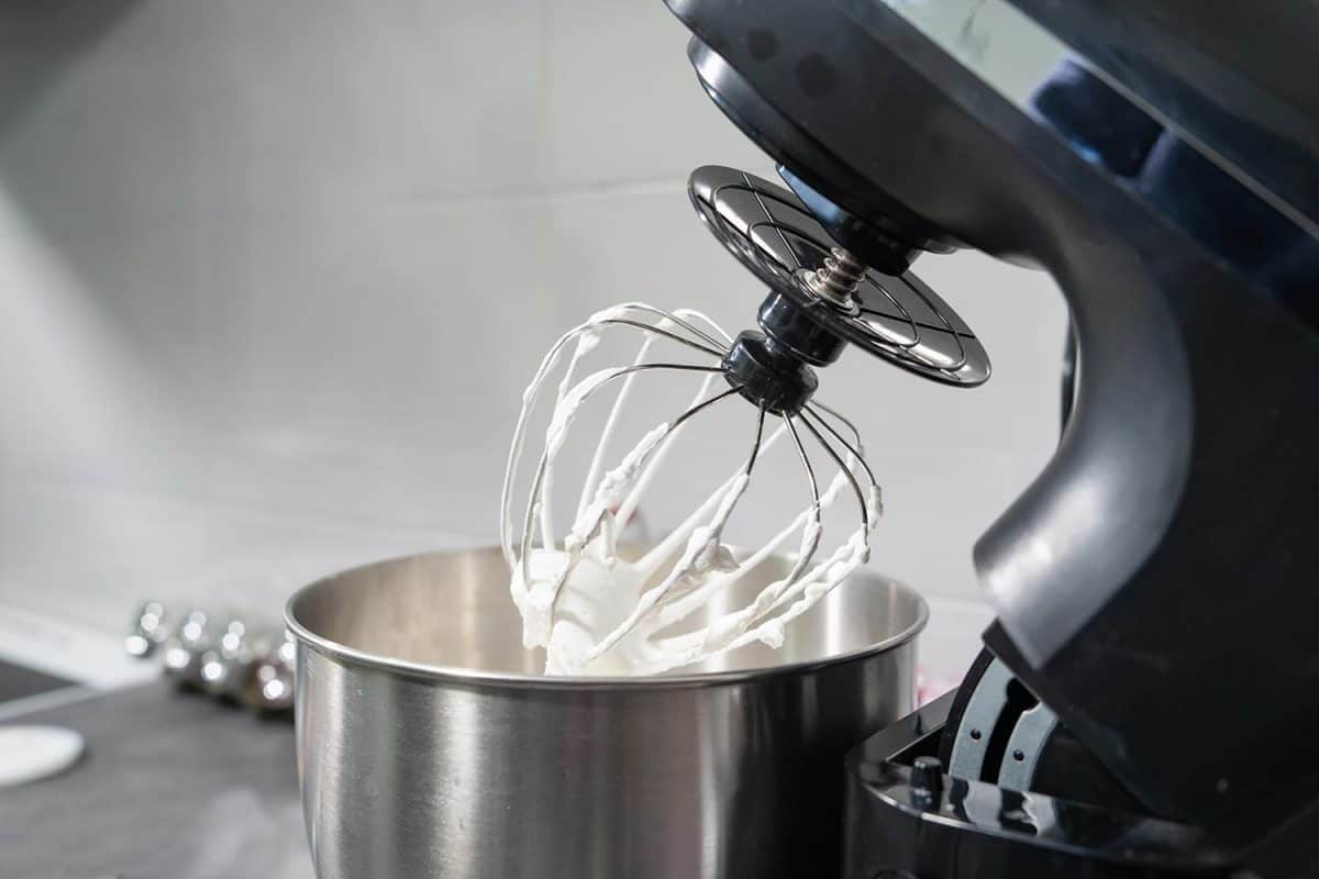 Black electric stand mixer on a table in the kitchen with white cream