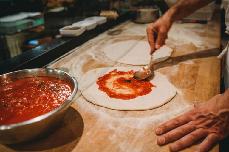 Chef spreading tomato sauce in the pizza dough, How Much Pizza Dough Per Pizza? [By Pizza Size]