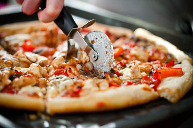 Close-up of pizza on cutting board that chef cuts into pieces with cutter, How Long Should Pizza Cool Before Cutting?