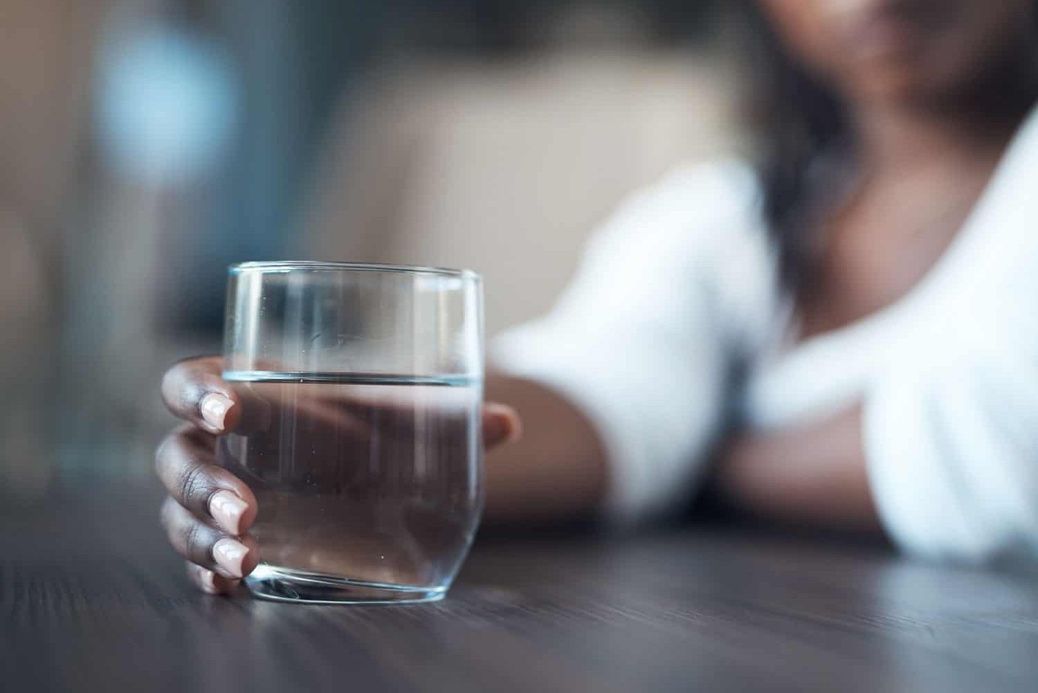 Cropped shot of an attractive young woman sitting alone and holding a glass of water at home