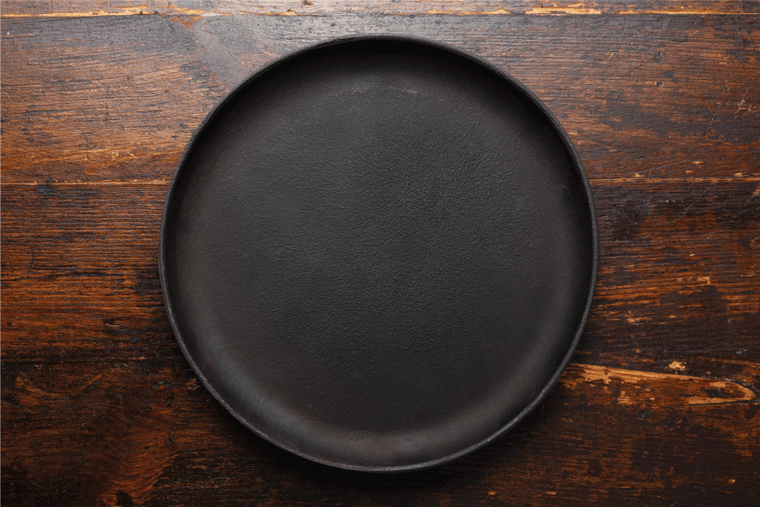 Empty round cast-iron pan for pizza on a brown wooden background