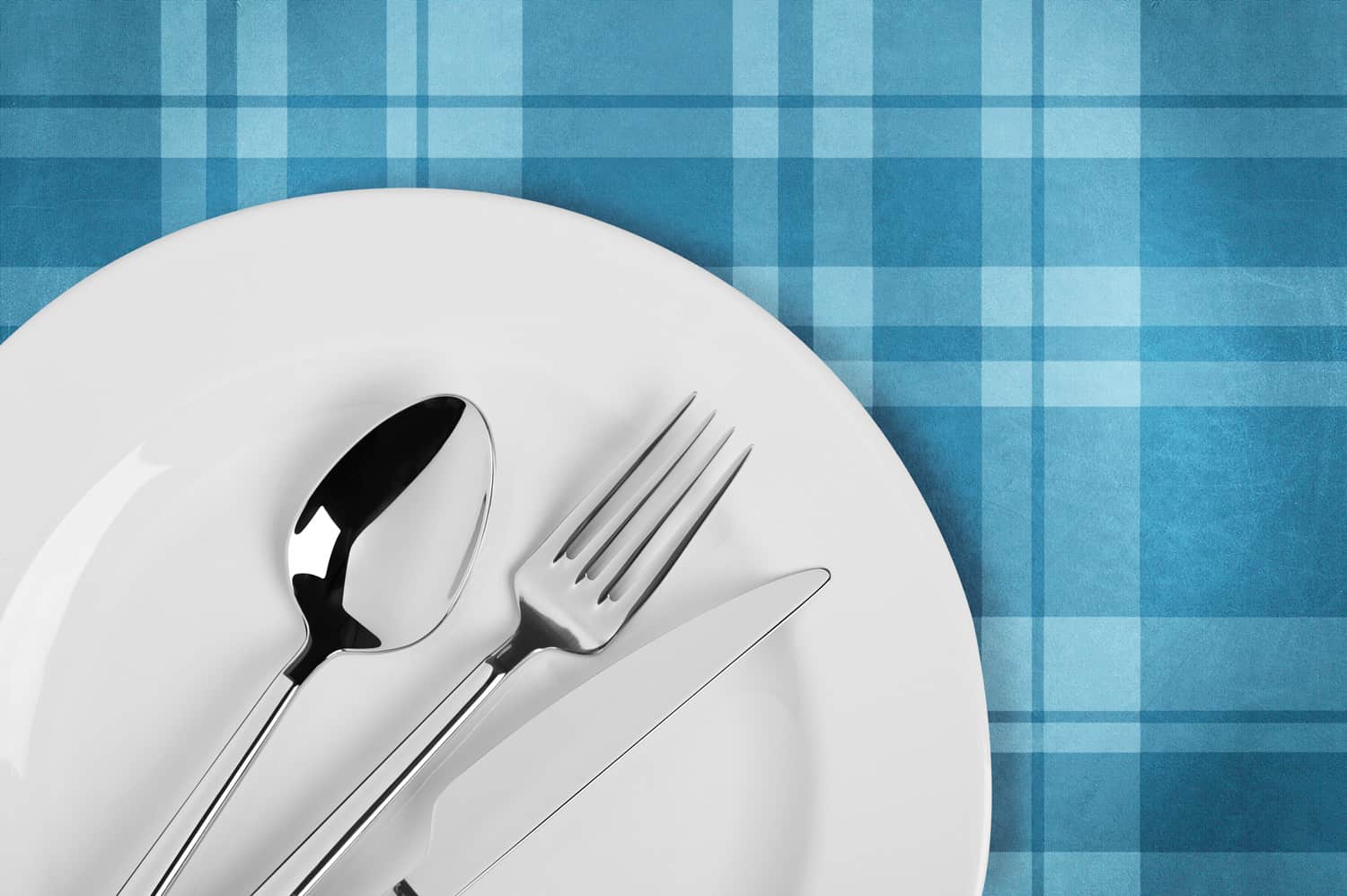 Empty white plate and fork,spoon and table knife on plaid tablecloth. Table setting Include clipping paths.