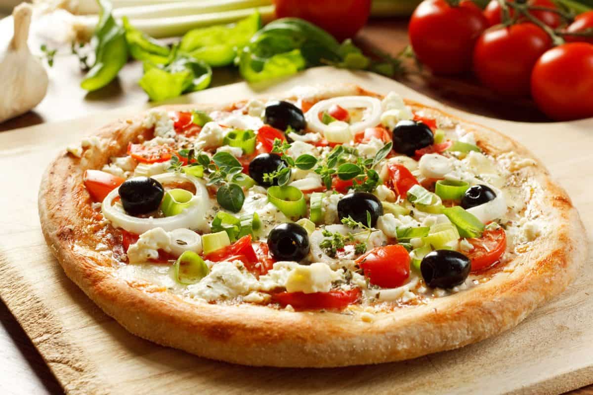 Fresh vegetarian Greek Style Pizza with olives, onion rings, feta cheese, mozzarella, tomatoes and fresh herbs