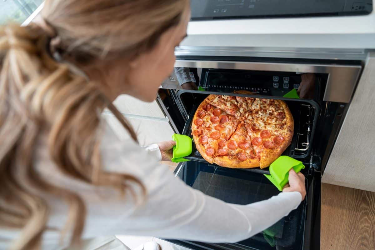 High angle view of unrecognizable woman taking out a fresh baked pizza from oven at home