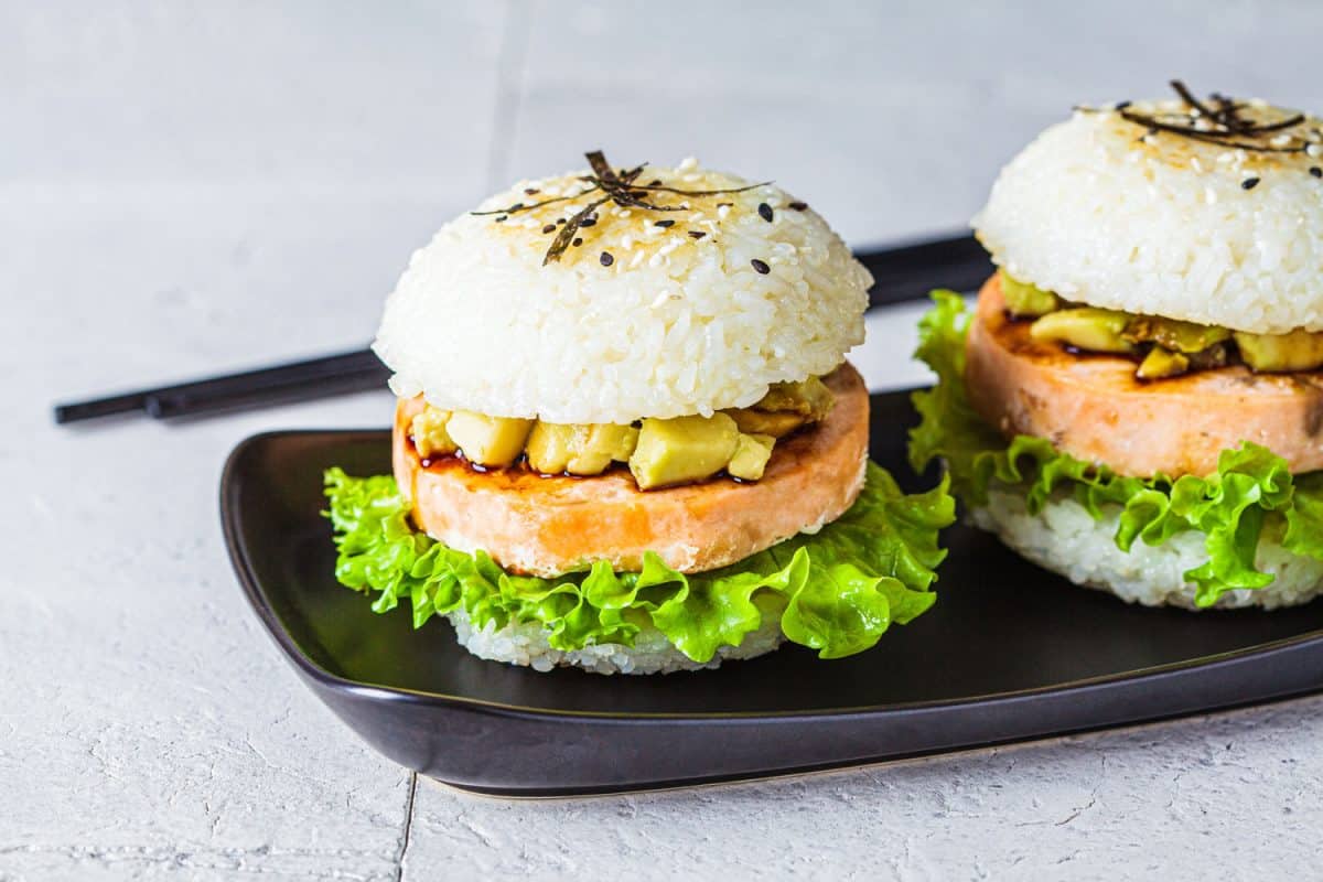 Rice burger with salmon cutlet, avocado and soy sauce, gray background.