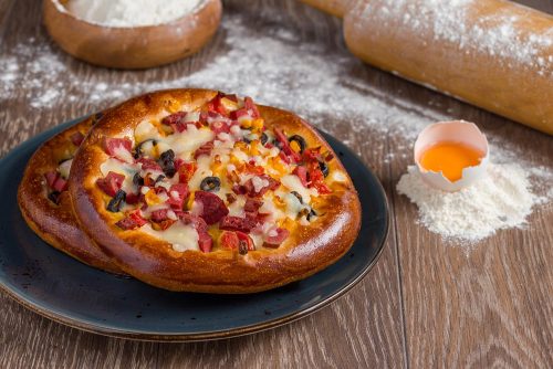 Small mixed pizza with pepperoni, sausage and cheese on wooden table