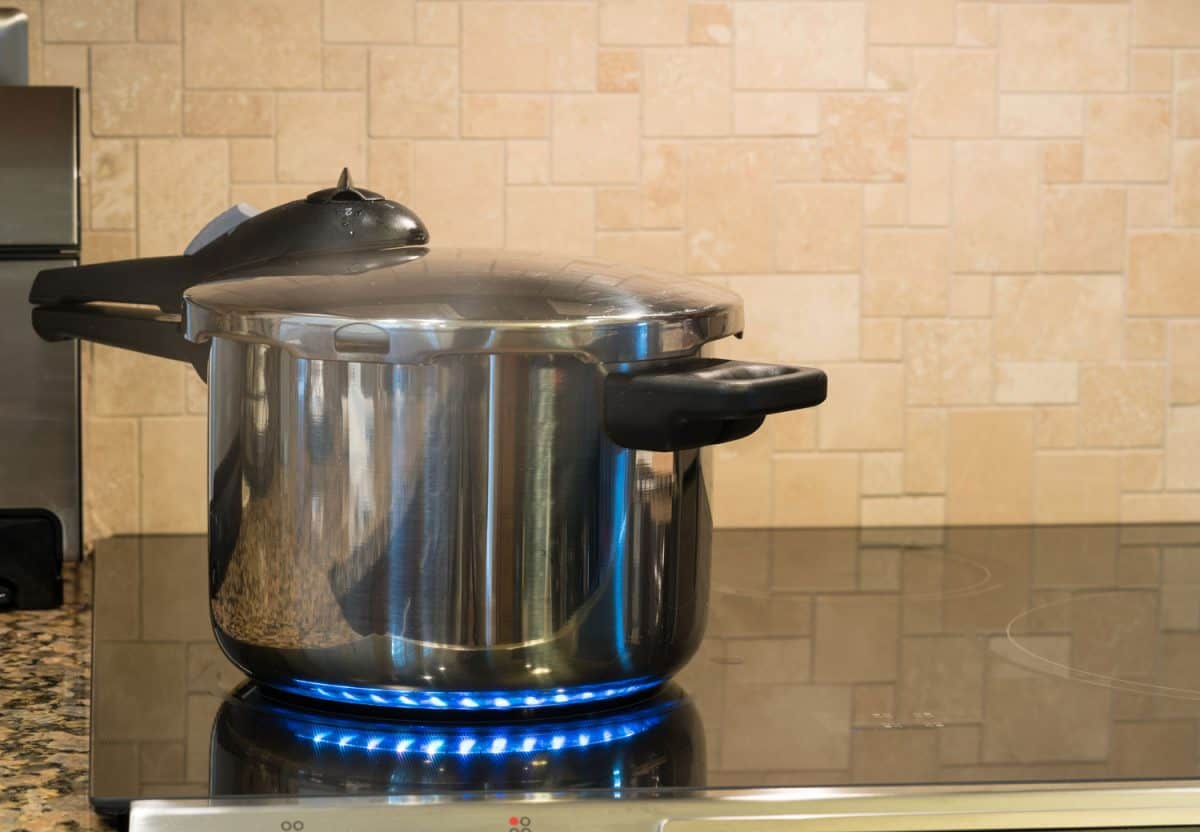 Stainless steel pressure cooker letting off steam on a modern induction cooking hob with glass top