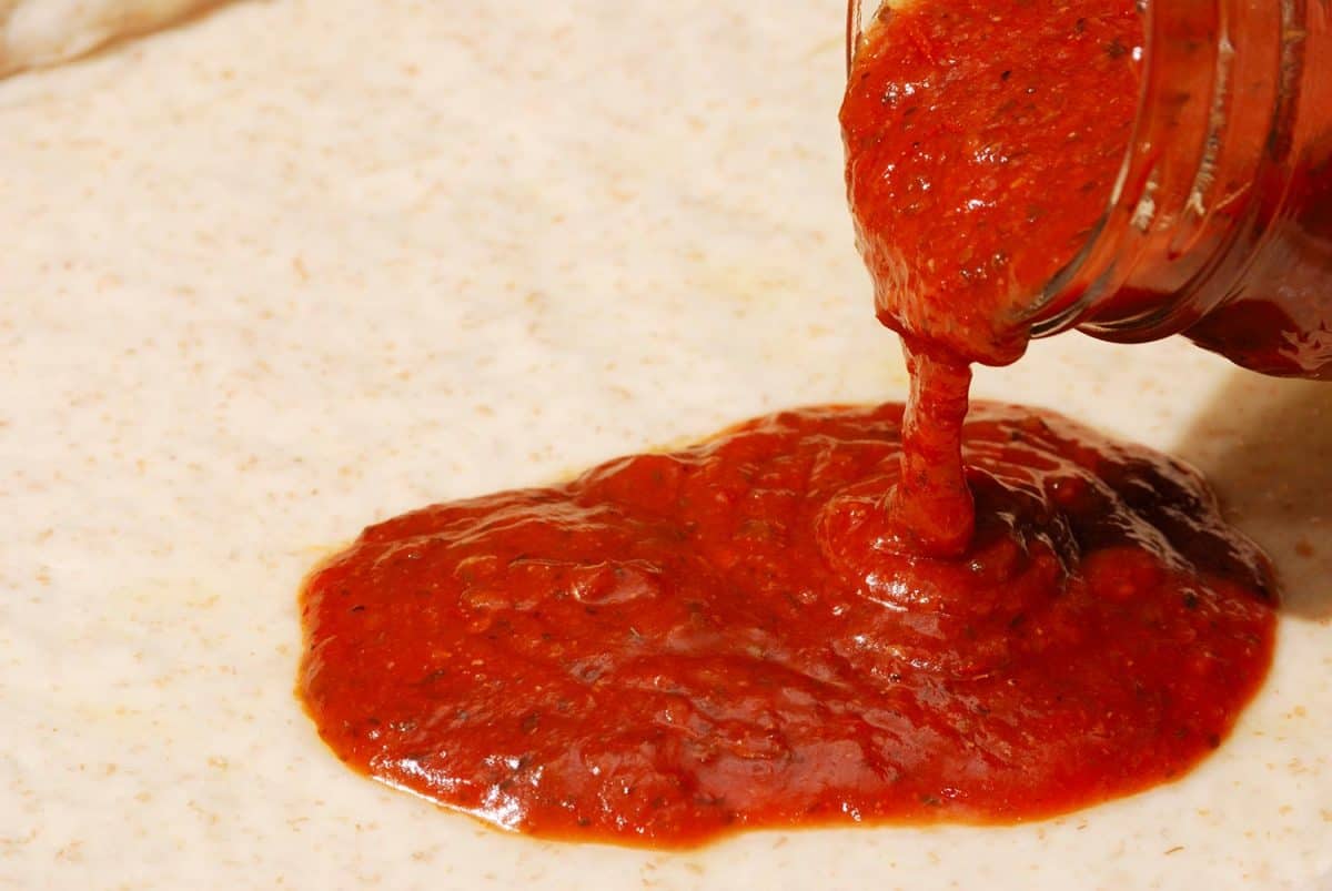 Tomato sauce is poured on pizza dough