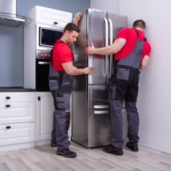 Two Young Male Movers Placing Steel Refrigerator In Kitchen, Can A Refrigerator Be Transported On Its Side Or Back?