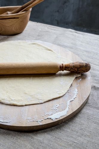 Wheat flour dough for making dumplings or pizza on a wooden board with a rolling pin