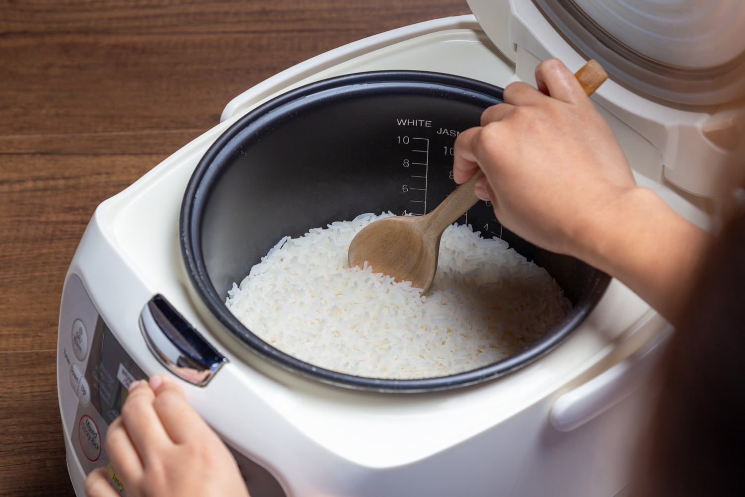 Woman hand is scooping jasmine rice cooking in electric rice cooker with steam