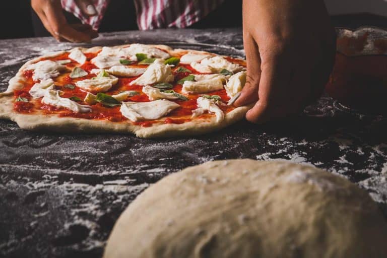 A woman hand making an Italian pizza on a floured surface, How Long Should Pizza Dough Rise?