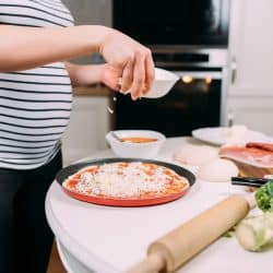 Woman pouring a generous amount of cheese, Should You Prebake Pizza Crust?