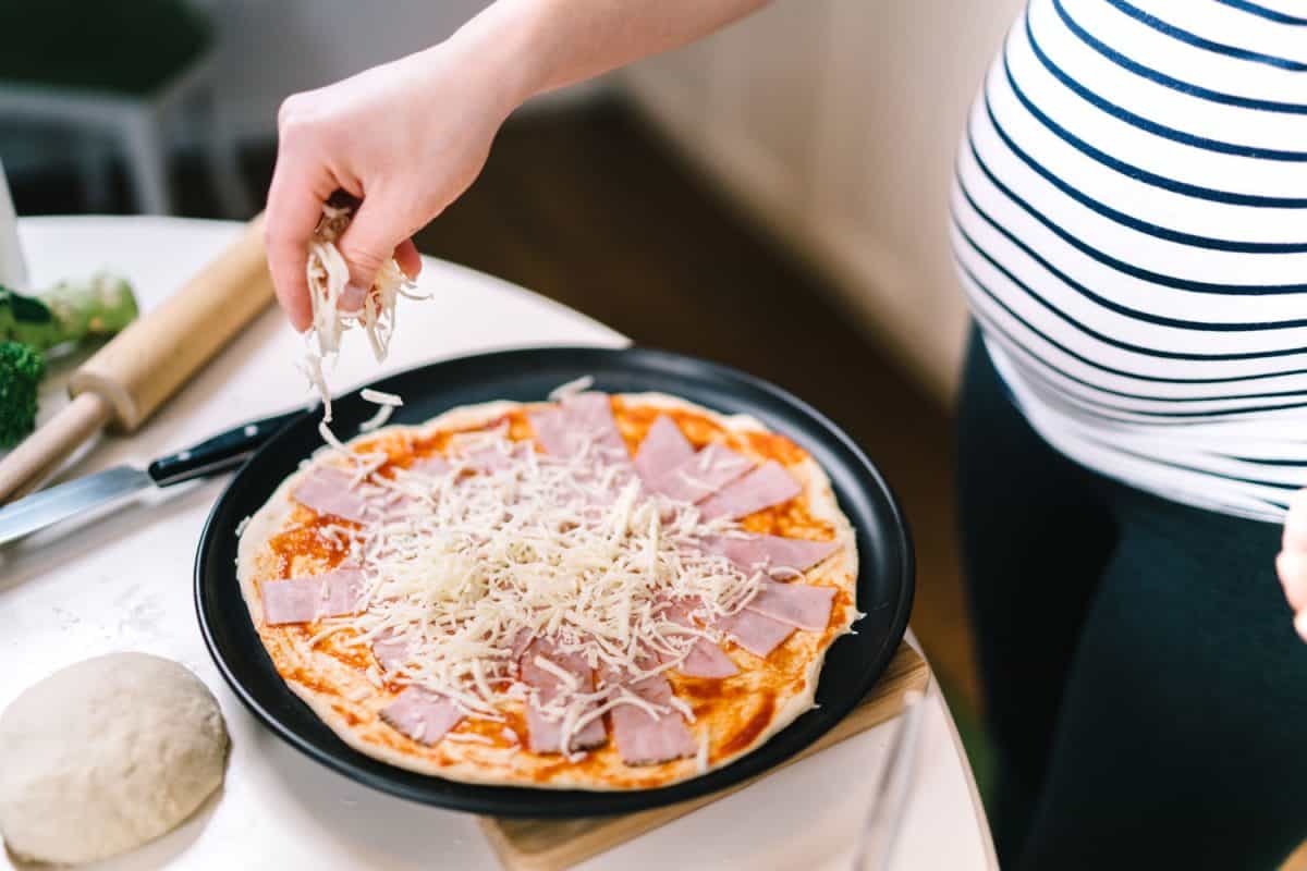 Woman pouring cheese on the pizza