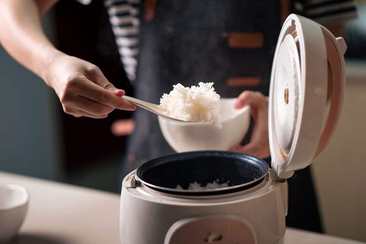 Woman taking out and serving fresh boiled fragrant jasmine rice from the rice cooker
