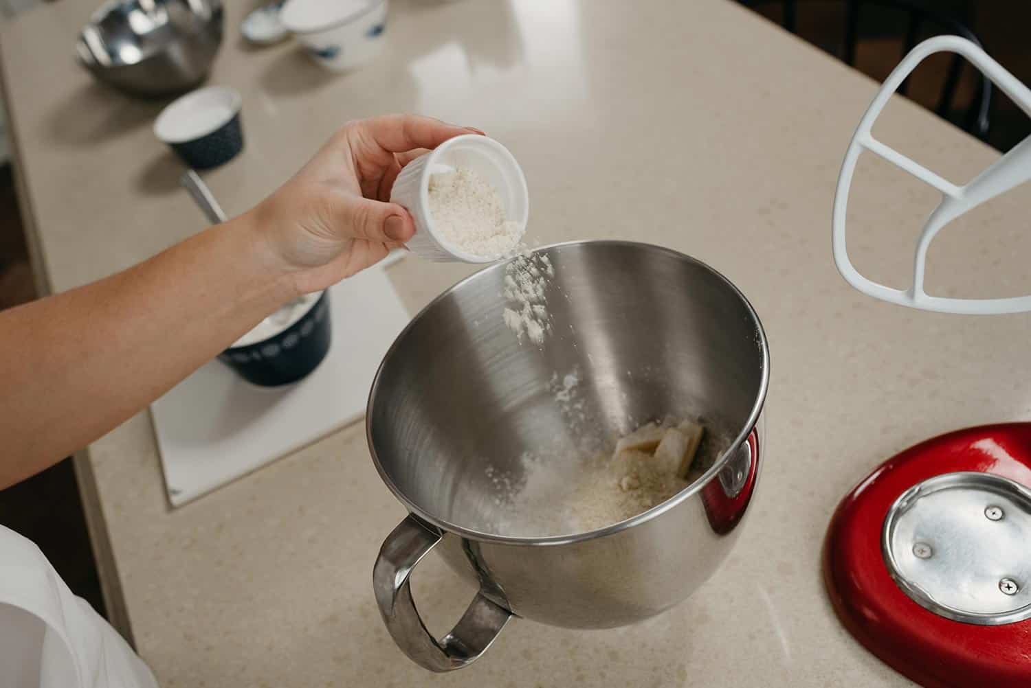 Woman who is putting an almond flour from the cup into the stainless steel bowl of the stand mixer