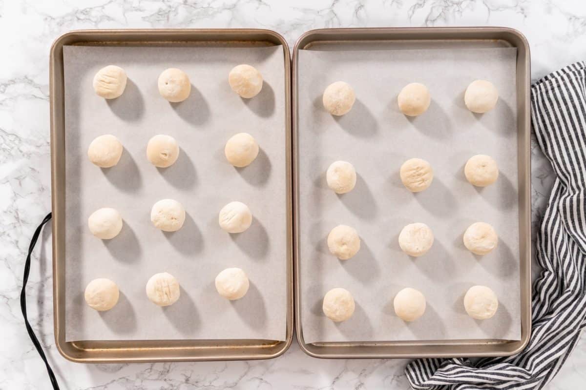 Flat lay. Rising frozen dinner rolls on a baking sheet lined with parchment paper.