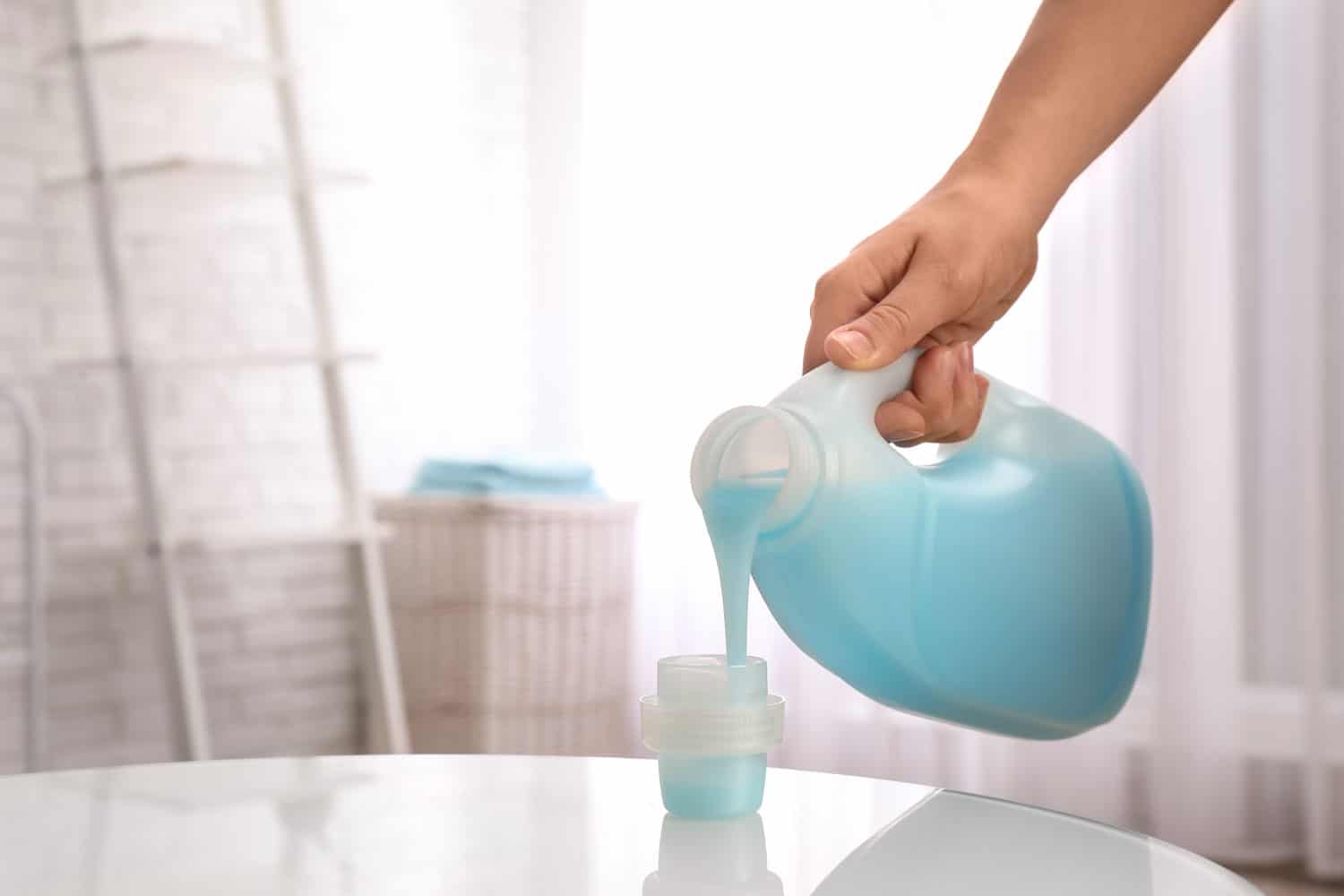 Woman pouring detergent into cap on table indoors,