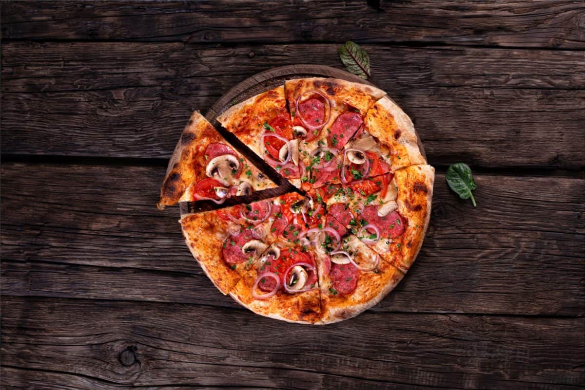 whole pizza with salami and mushrooms flat lay on a dark background in a rustic style.