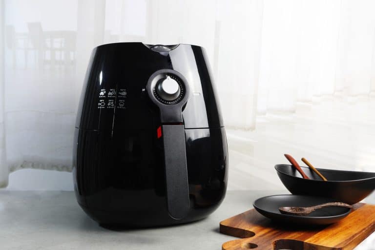 A black air fryer with a chopping board on the side, Can You Put A Bag Of Popcorn In An Air Fryer?