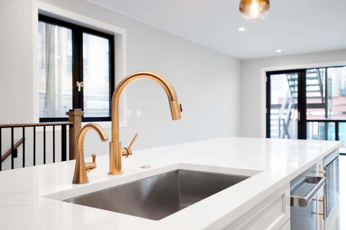 A bronze coated kitchen faucet in a white kitchen