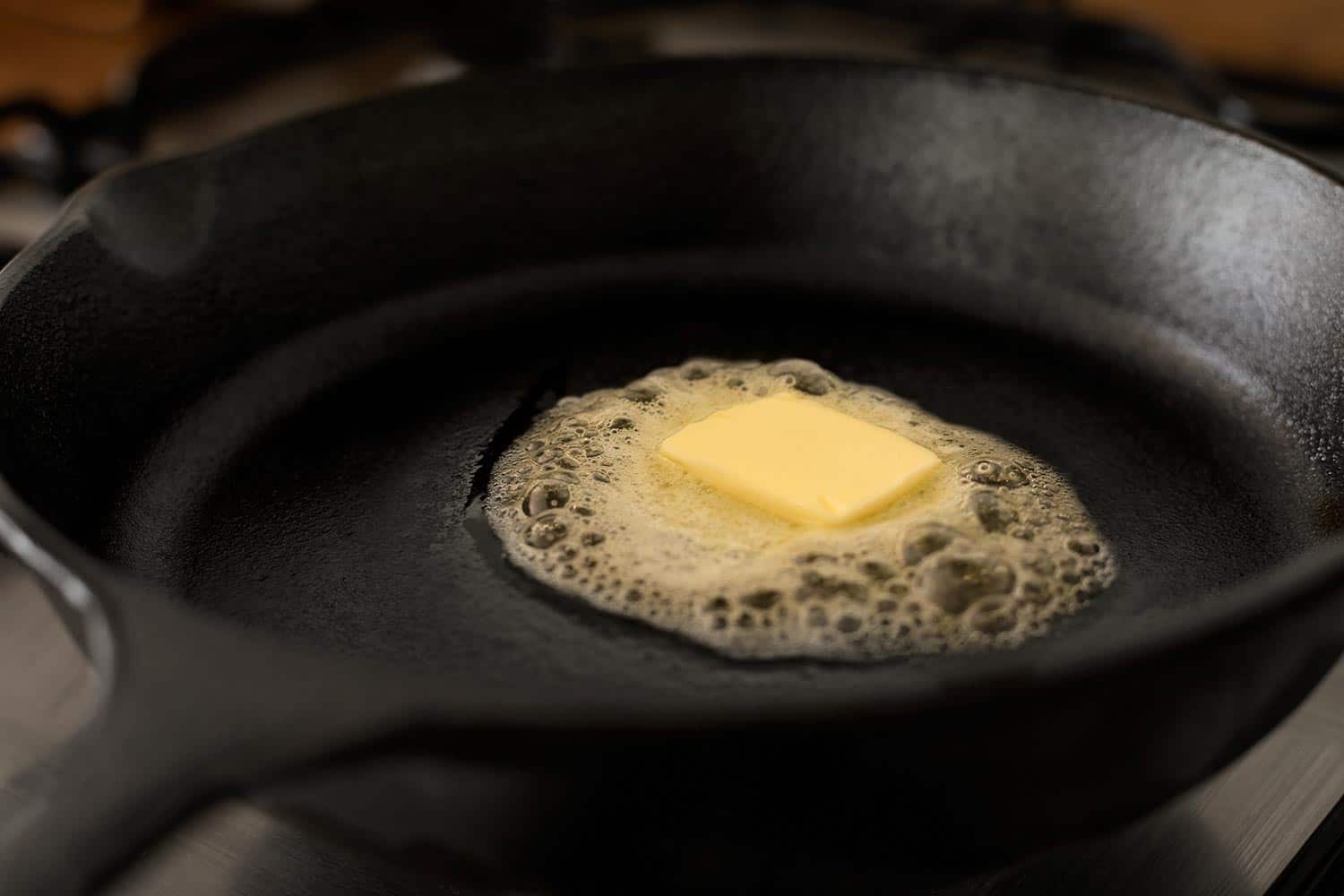 A butter pat melting on a black cast iron frying pan