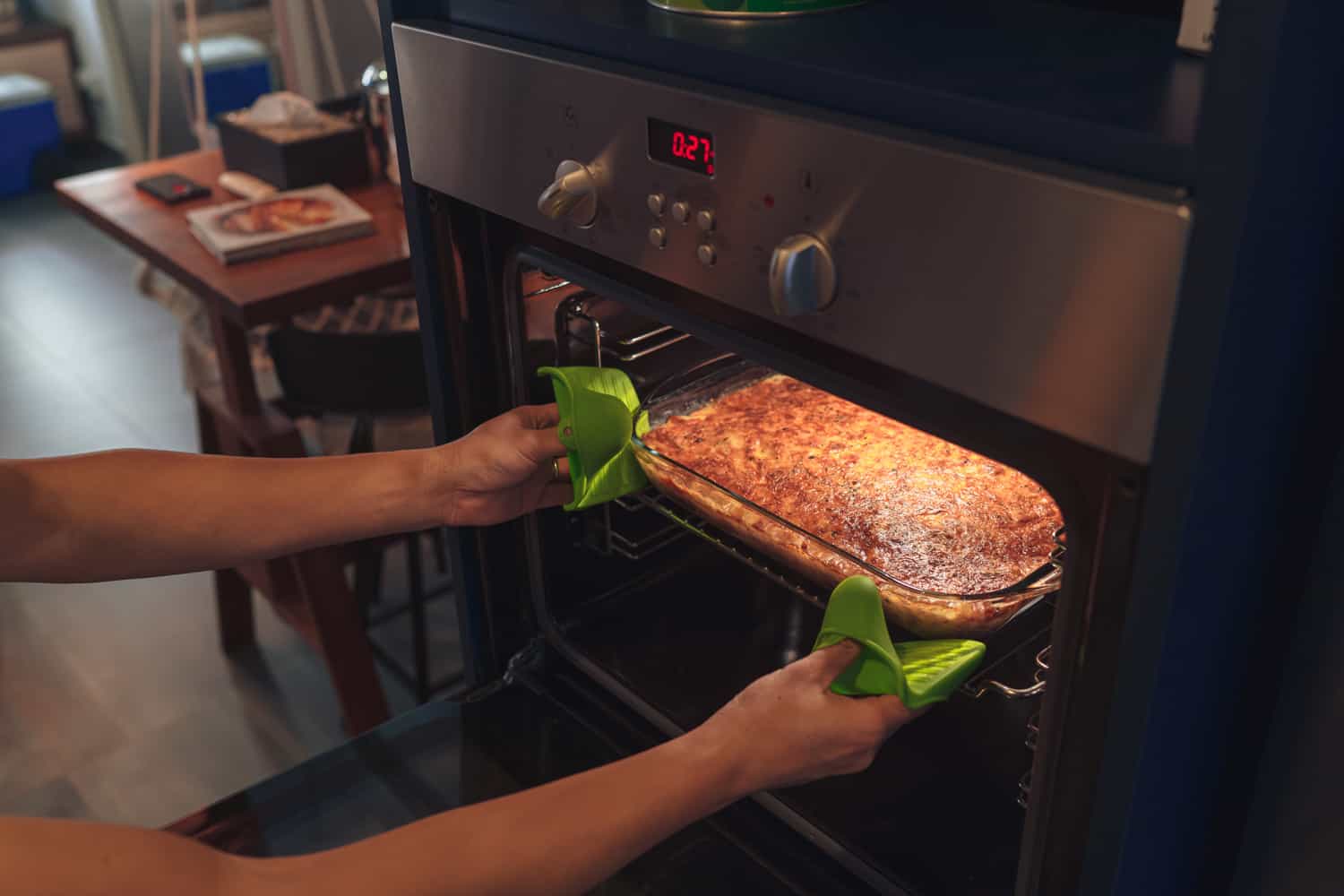 A pair of hands retrieving freshly baked lasagne from the oven