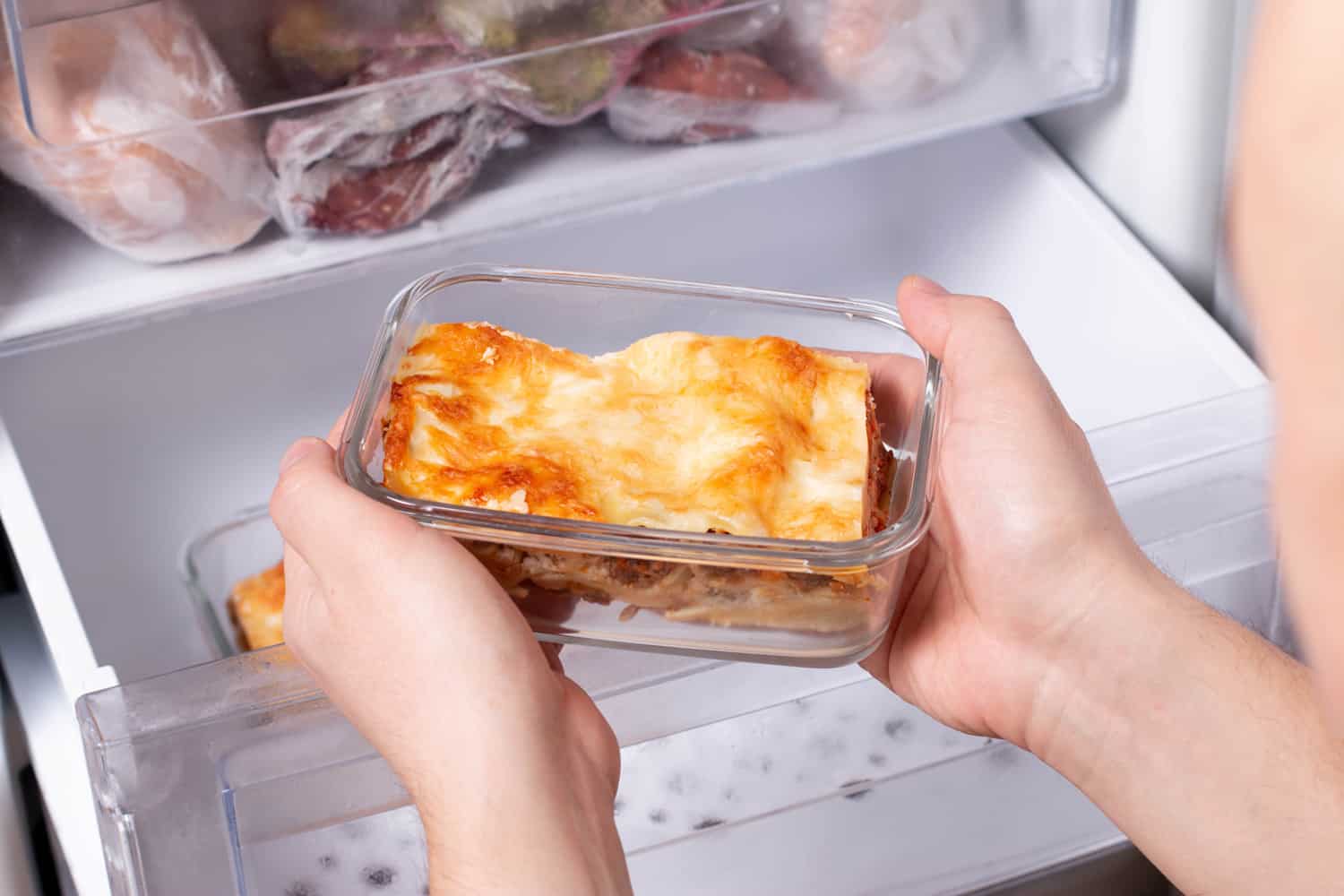 A person is taking a container of frozen casserole or lasagne out of the freezer