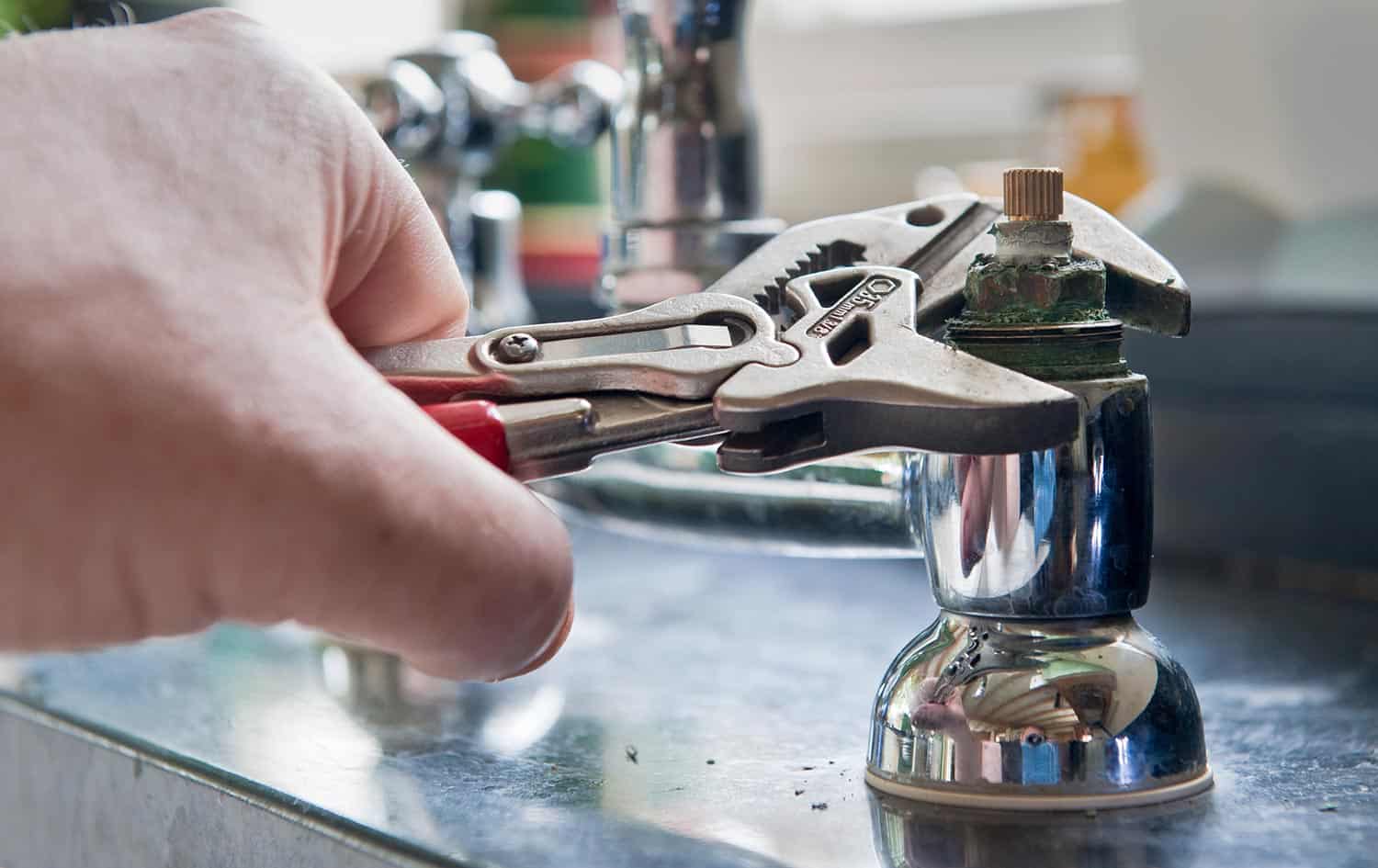  A plumber uses adjustable grips to remove a worn insert from a set of kitchen taps