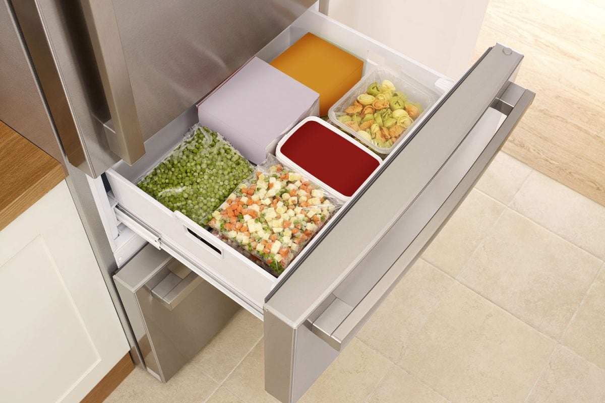 An opened drawer of a refrigerator filled with vegetables and other peas