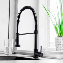 Black kitchen faucet on the silver sink near the glass of wate - Do Kitchen Faucets Come With Drains