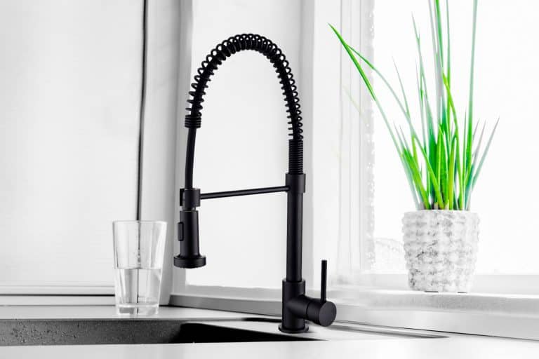 Black kitchen faucet on the silver sink near the glass of wate - Do Kitchen Faucets Come With Drains