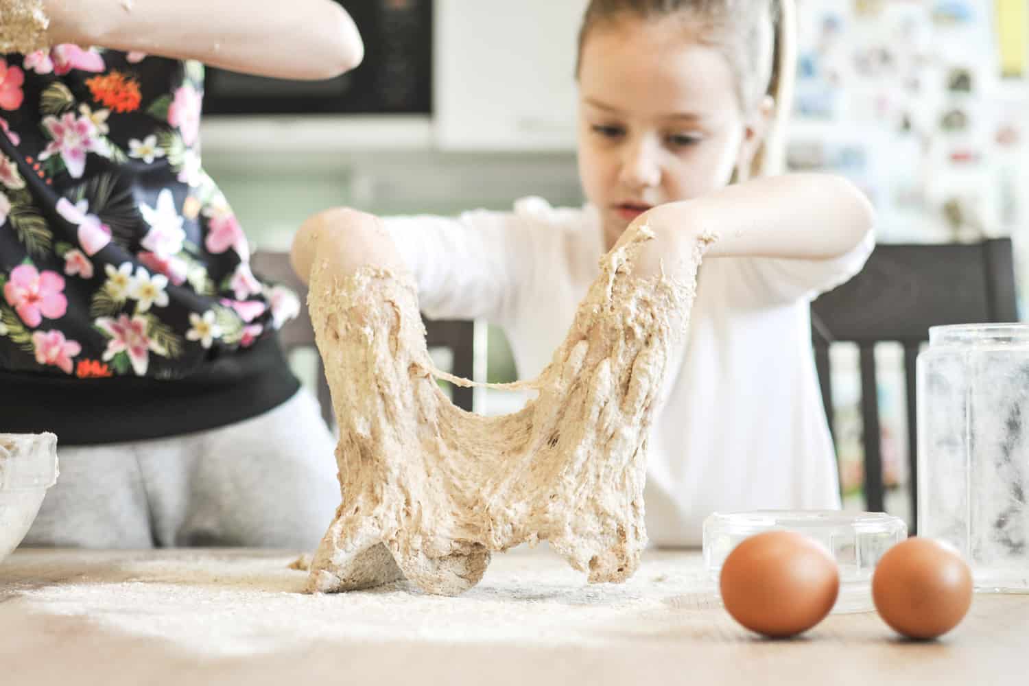 Cute little girls having fun while making a dough for a bread or pizza in a domestic kitchen.