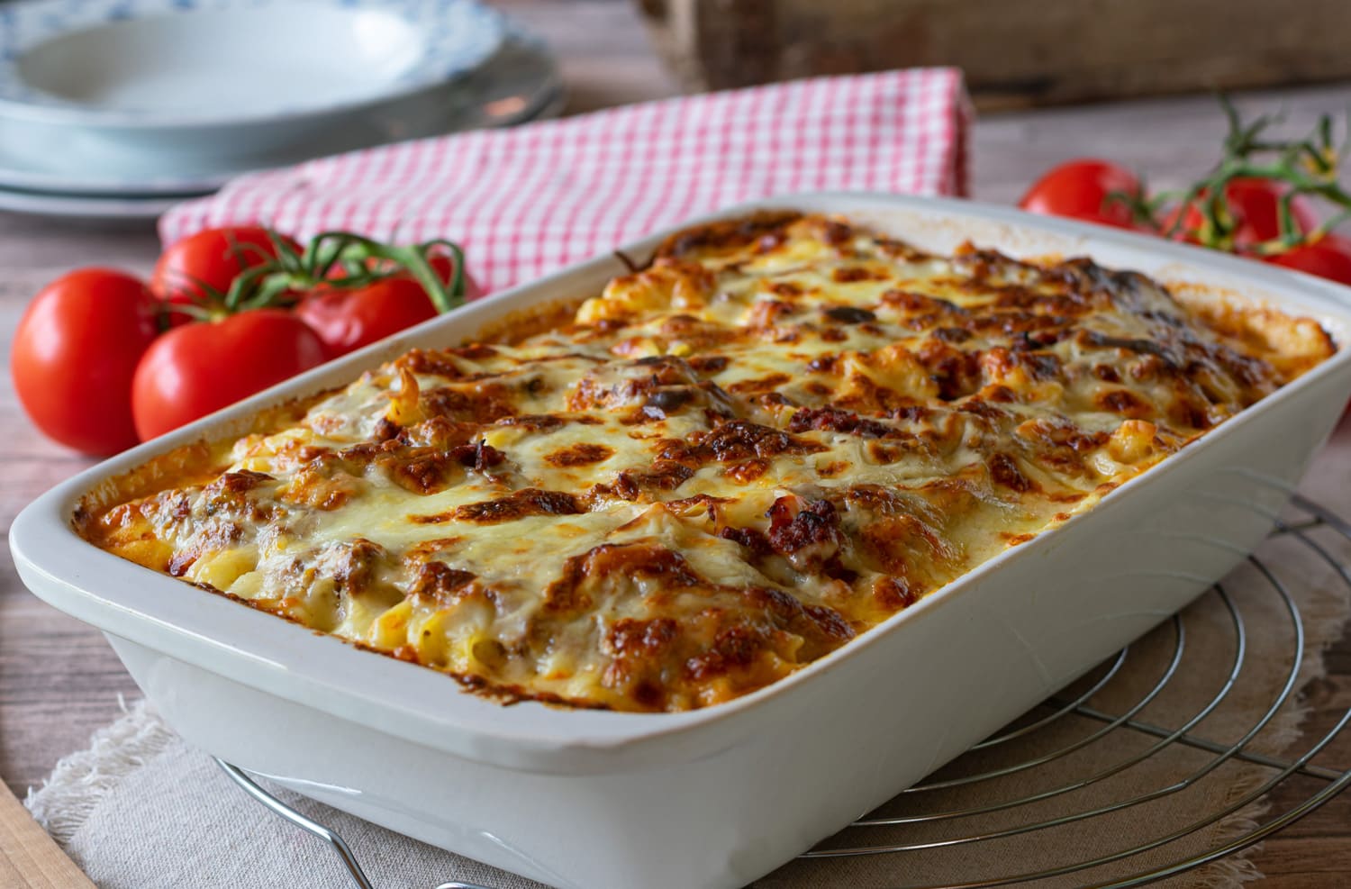 Delicious homemade italian gratin dish with home cooked bolognese sauce and bechamel sauce topped with mozzarella cheese and served in a white baking dish on rustic table background.