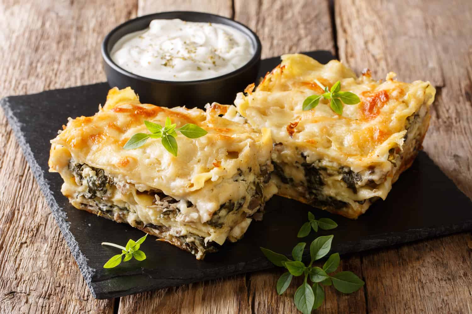 Delicious lasagna with chicken breast, porcini mushrooms, cheese, herbs and bechamel sauce close-up on a slate plate on a wooden table.