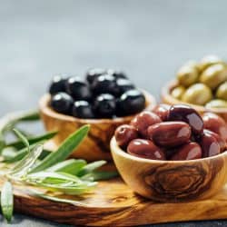 Different types of olives in olive wooden bowls and olive oil over wooden cutting board and fresh olive leaves, How Long Do Olives Last In The Fridge?