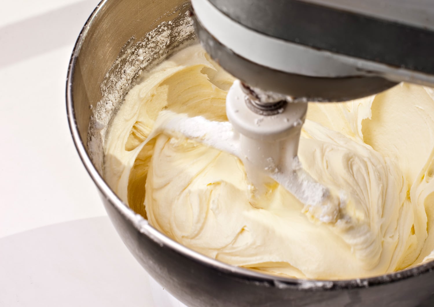 Electric mixer mixing yellow lemon cream cheese cake frosting.