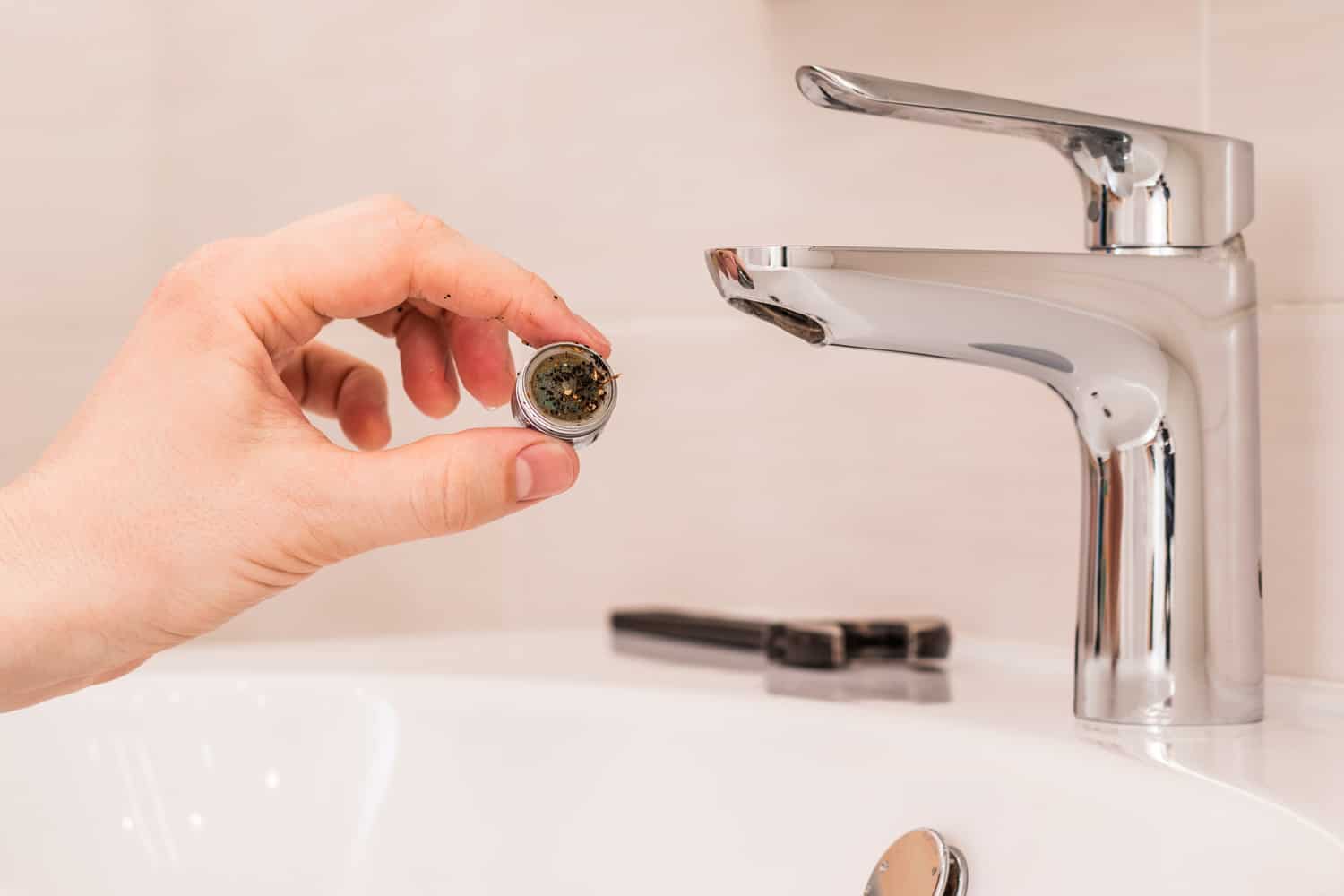 Faucet cleaning. Person's hand holds a clogged aerator. Sediment in water