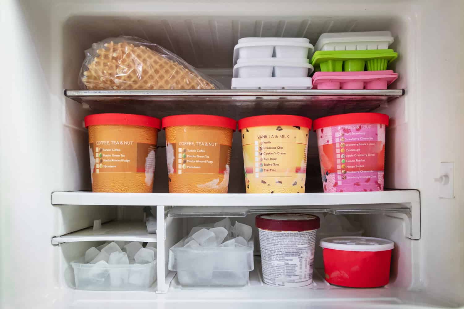 Full of bucket container ice creams flavors and ice cubes in freezer.