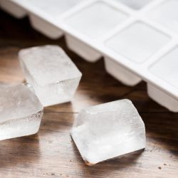 An ice cube tray and three lose ice cubes on the dark wood, Can You Consume Ice From A New Refrigerator?