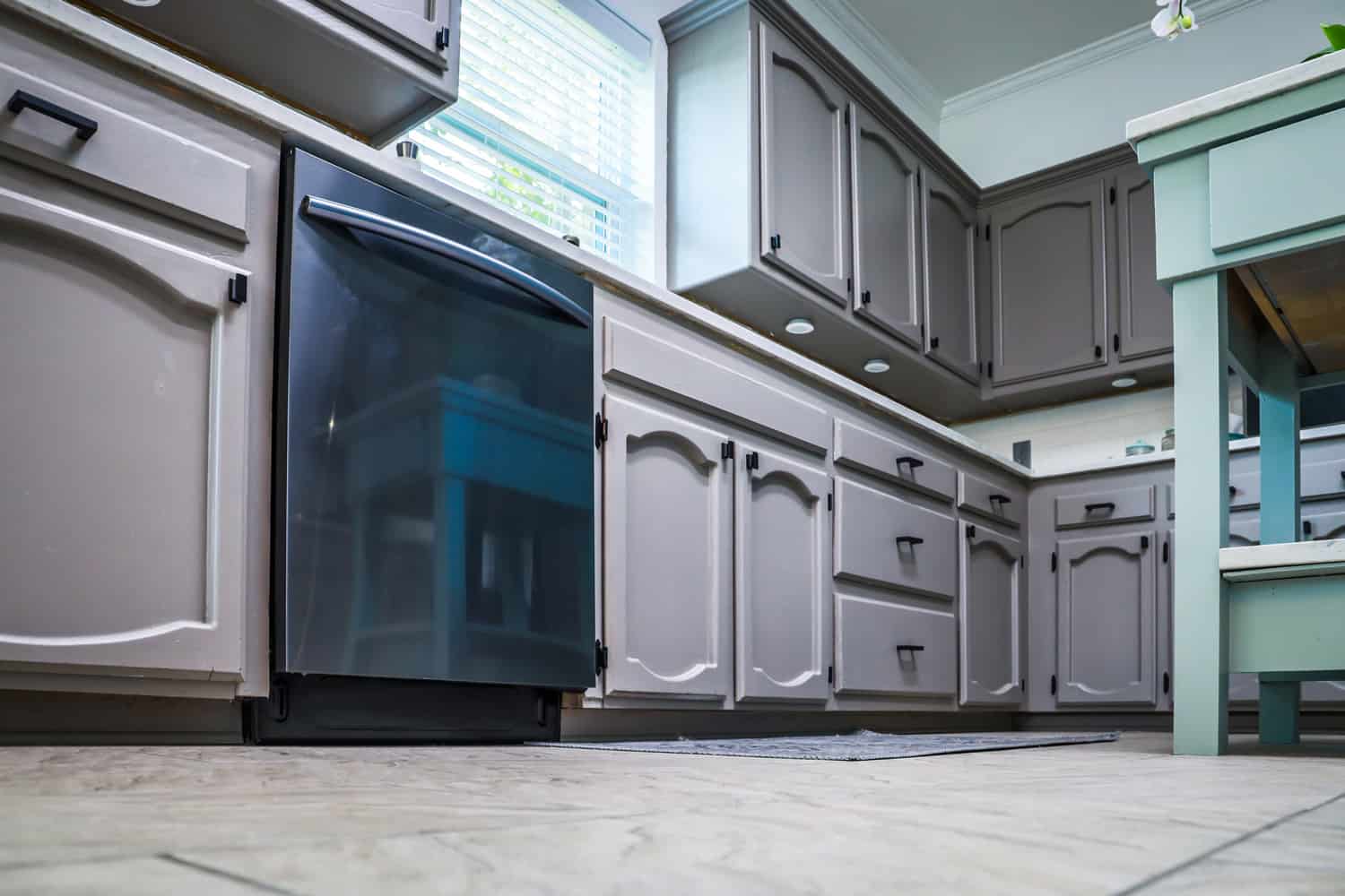 Low angle view of a renovated kitchen in an older home with painted gray cabinets, marble countertops, a small portable island and a tiled floor.