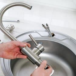 A plumber hand holds a new faucet for installing into the kitchen sink, How Long Does It Take To Replace A Kitchen Faucet