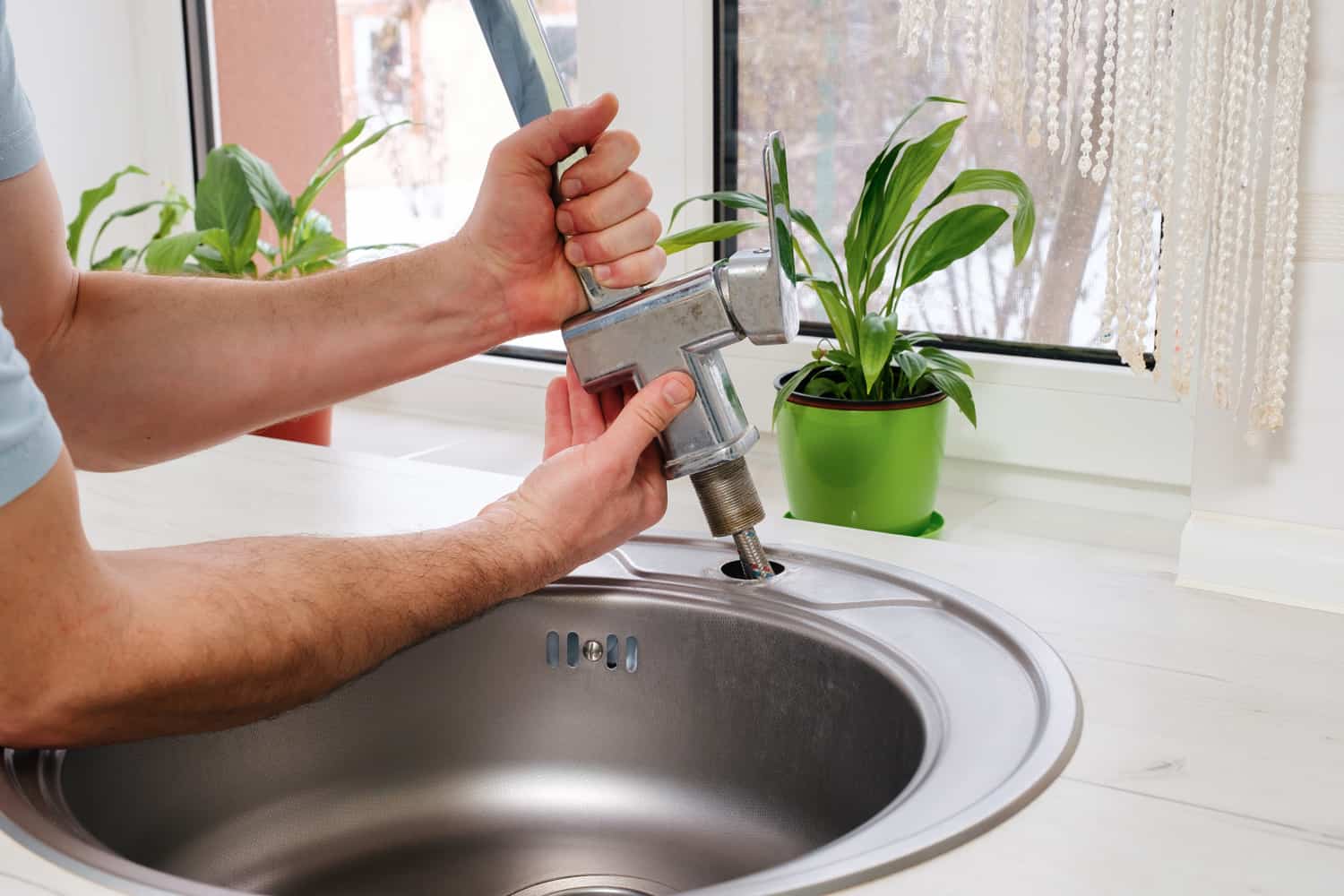 Plumber hands removes the old faucet from the kitchen sink for replacing it with a new one