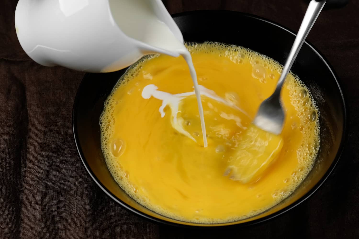 Pouring milk and mixing eggs with fork. Cooking Scrambled eggs, omelette
