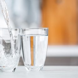 Pouring of fresh water into glass on table in kitchen, Do Drinking Glasses Wear Out? [And How To Prevent That]